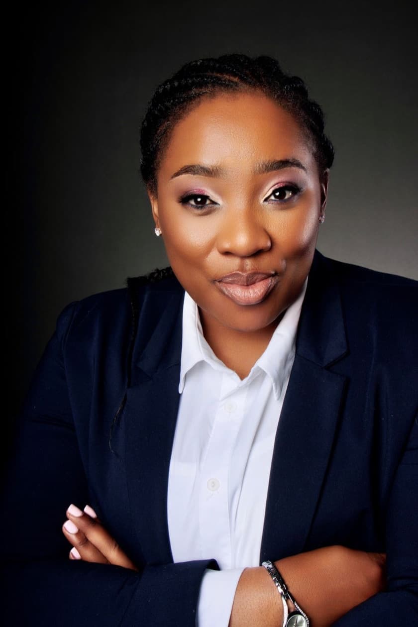 Adv. Miliswa Mokoteli in a navy blazer and white shirt, arms folded, against a dark background