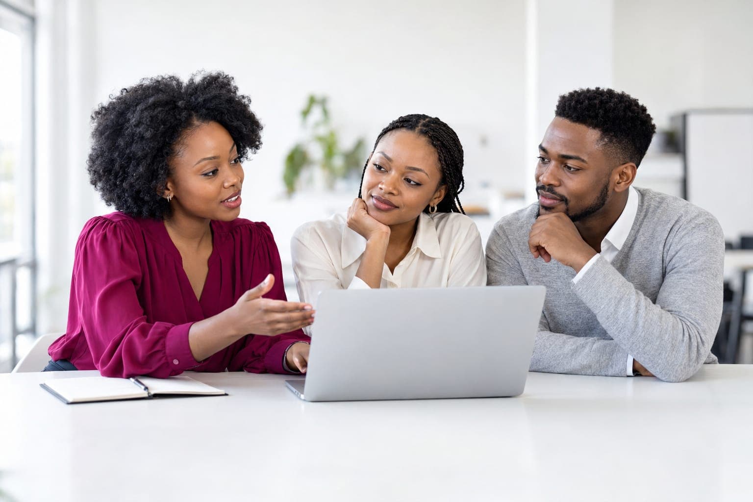 Facilitator in a burgundy blouse talking two young colleagues through work on a laptop